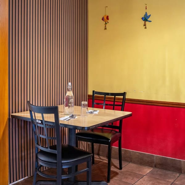 A cozy restaurant corner with a wooden table, two black chairs, and colorful wall decorations.