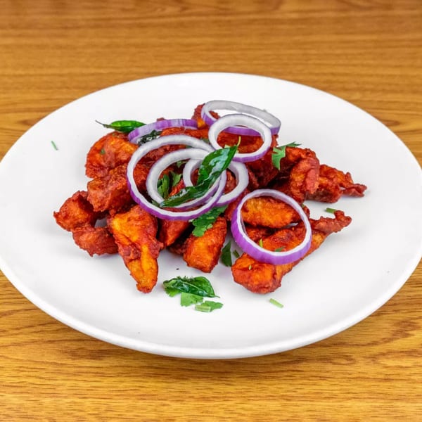 A white plate filled with crispy, red-orange fried chicken pieces, garnished with red onion rings and green herbs.