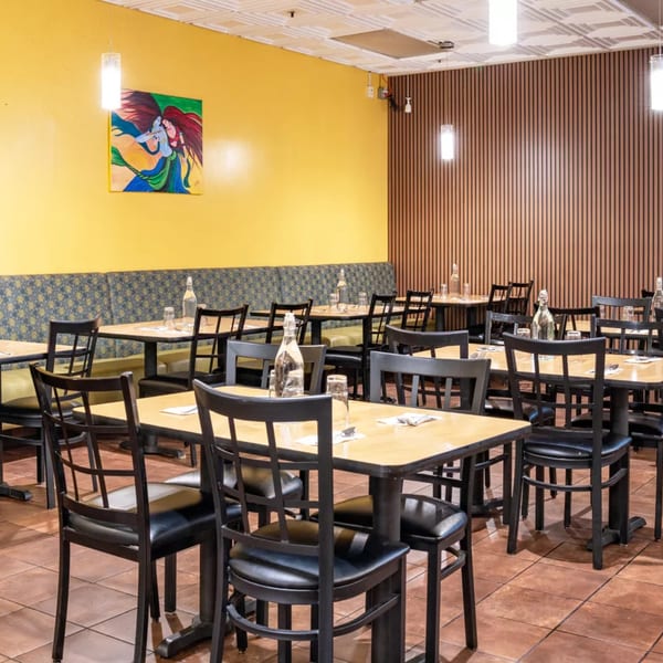 Restaurant dining room with yellow walls, patterned banquettes, light wood tables, and black chairs.