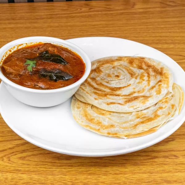A white bowl of chicken curry with two paratha flatbreads on a white plate.