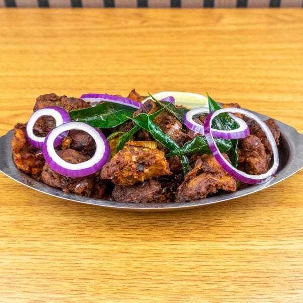 Spicy chicken fry with red onion rings, green chilies, and curry leaves on a metal plate.