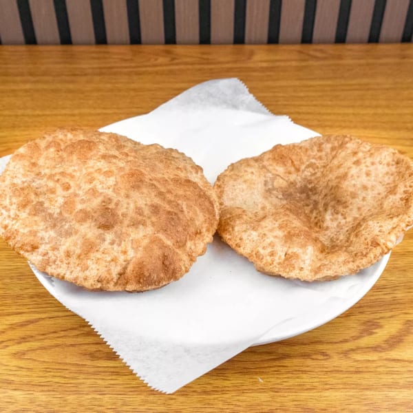 Two golden-brown fried dough pastries, likely puri or bhatura, on a white plate with parchment paper.