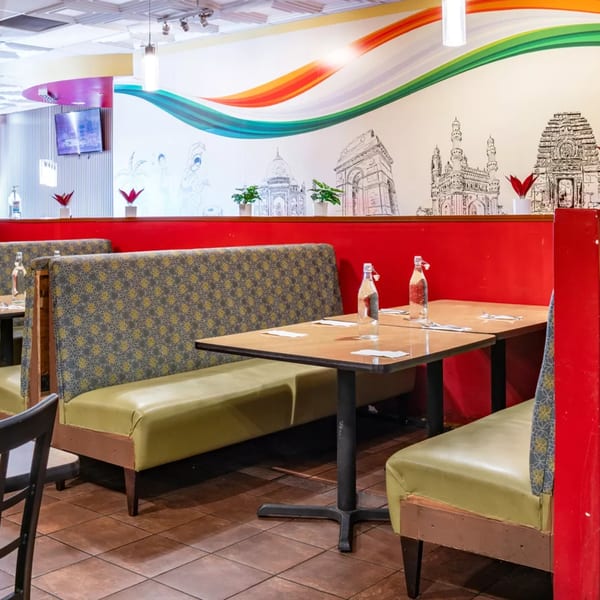 Restaurant interior with red booths, patterned seating, and a mural of Indian landmarks on the wall.