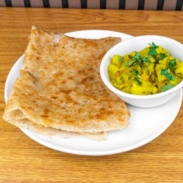 Crispy dosa served with a side of yellow potato curry, garnished with fresh cilantro on a white plate.
