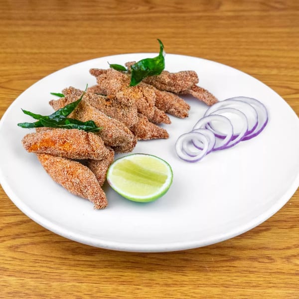 Crispy fried fish pieces with curry leaves, a lime wedge, and red onion rings on a white plate.
